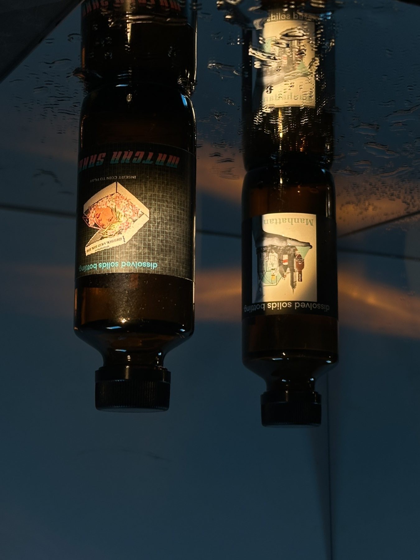 Two Dissolved Solids bottled cocktails in low light, Matcha Sakura and Manhattan