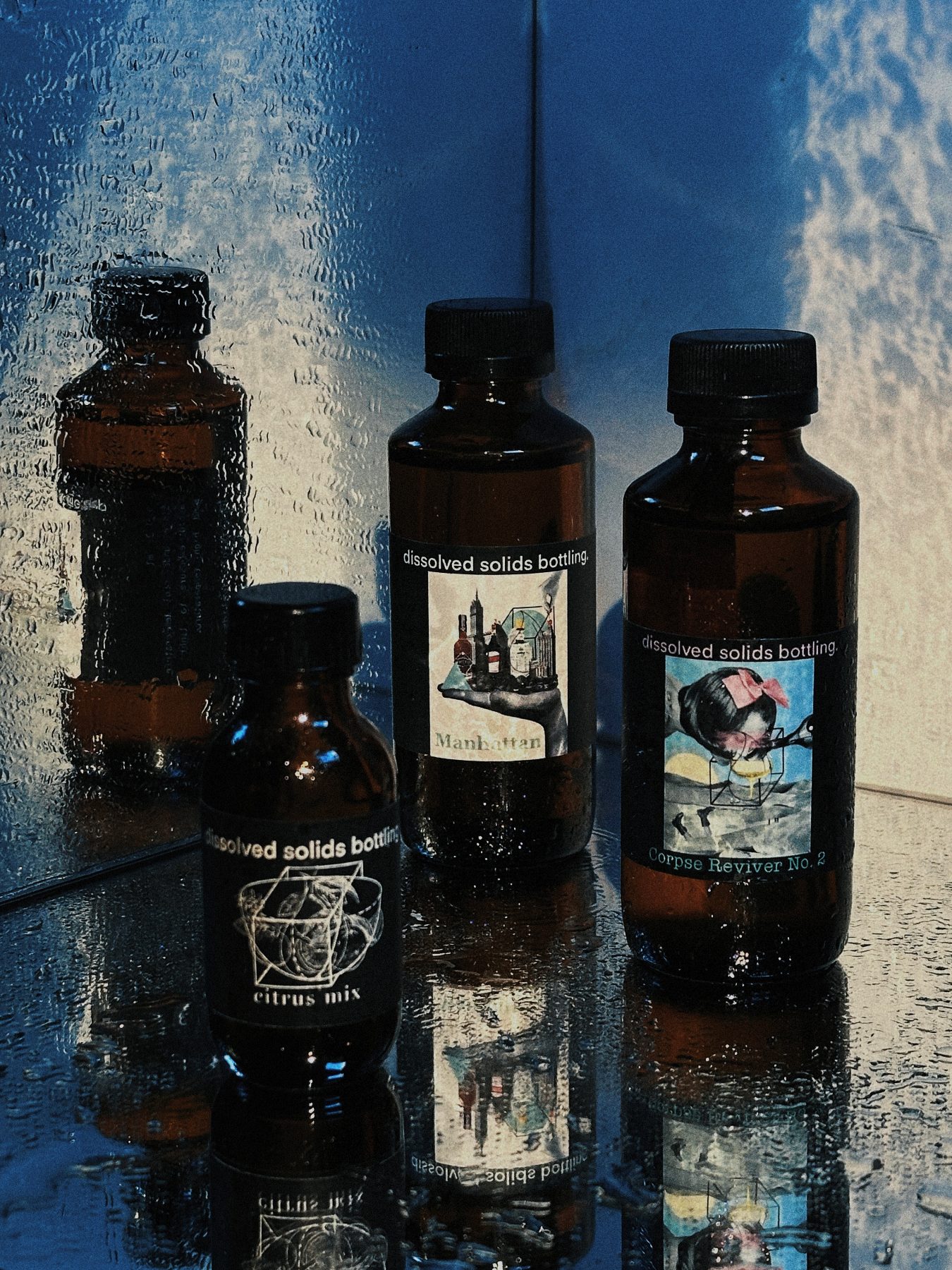 Lineup of Dissolved Solids bottled cocktails reflected against a sky backdrop with droplets