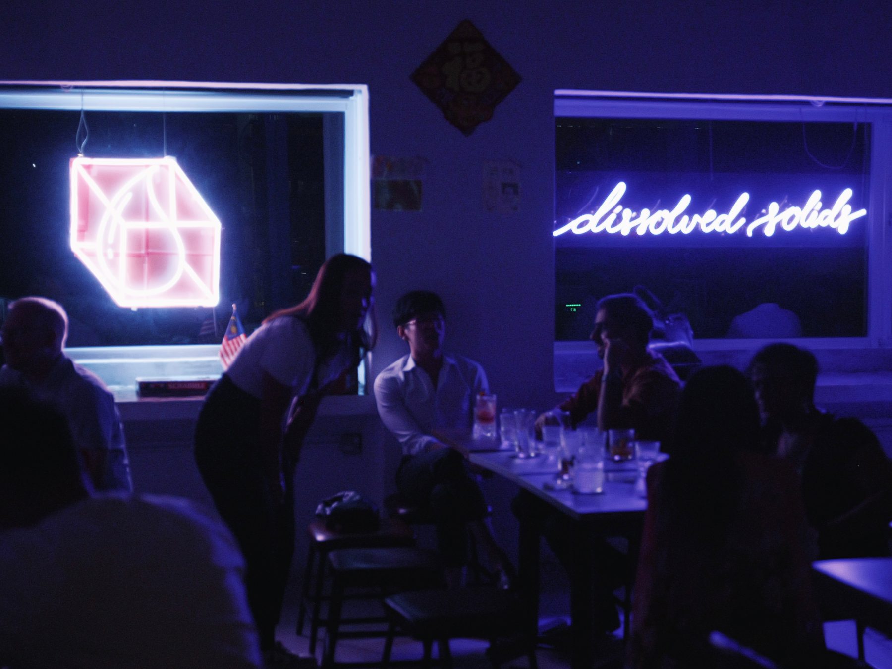 The Dissolved Solids bar at night with the pink cube neon and cursive sign, friends at a table