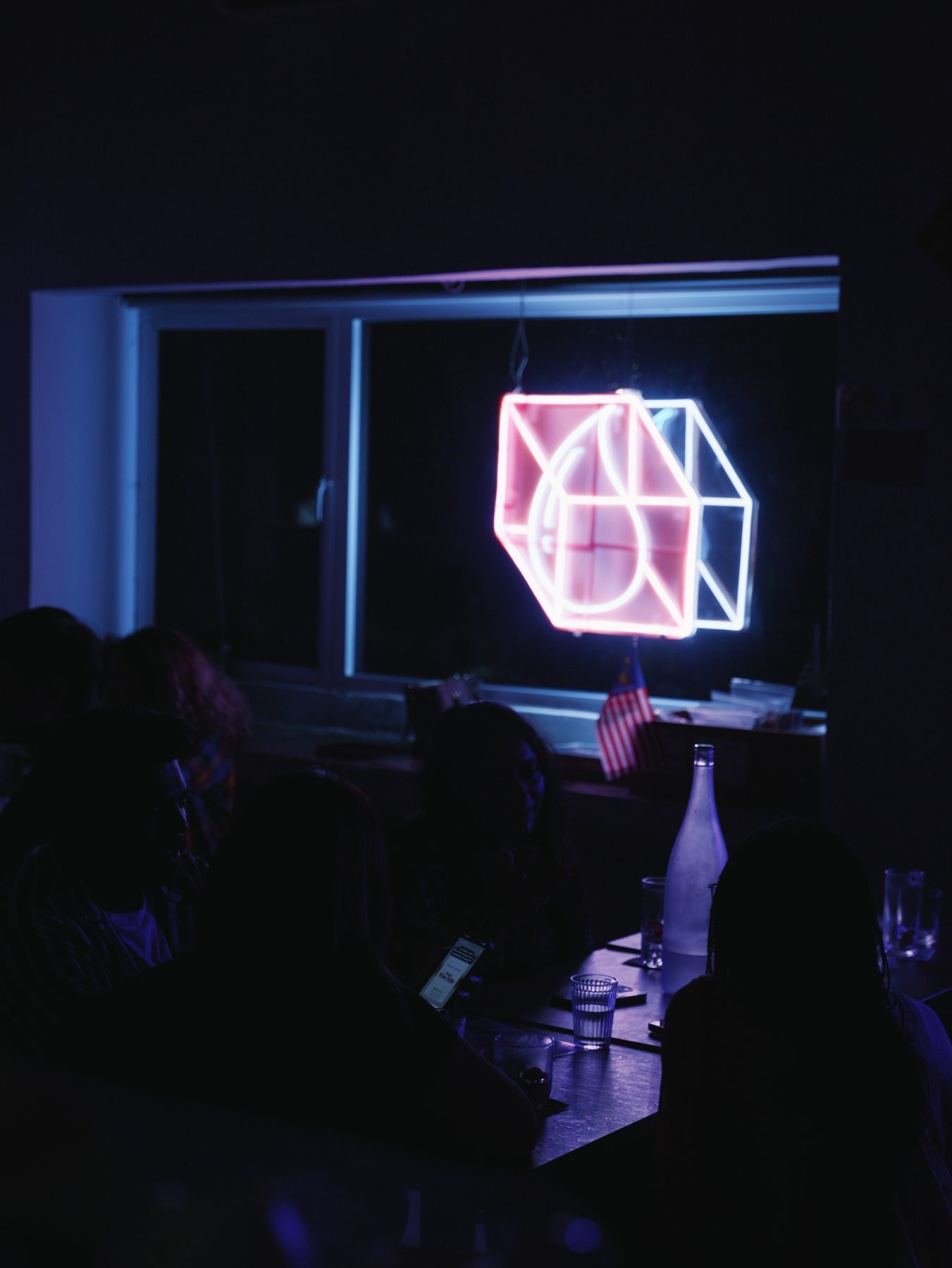 Pink cube neon logo glowing on the bar countertop at night, Dissolved Solids
