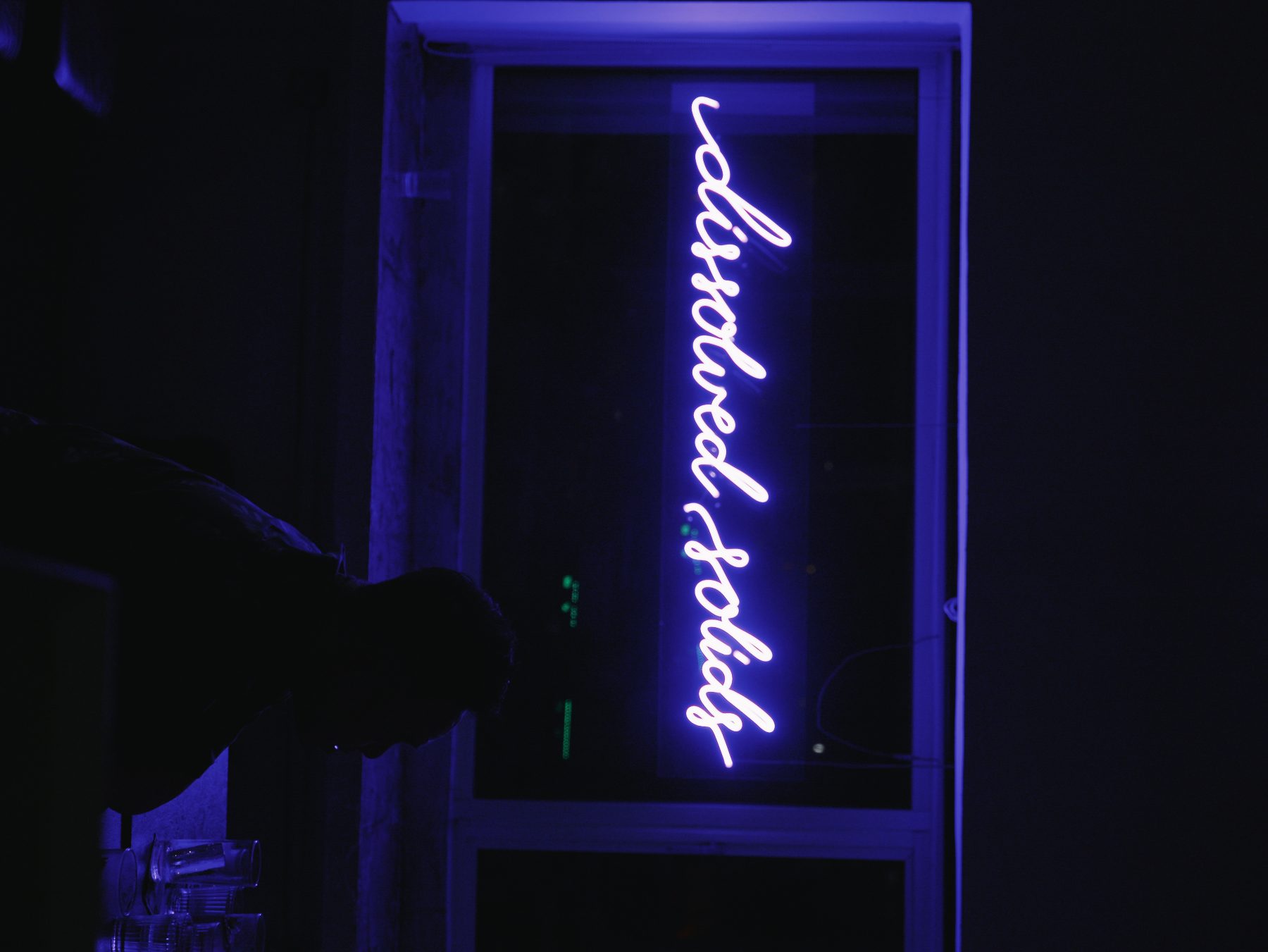 The 'dissolved solids' cursive blue neon sign on the bar's glass doorway