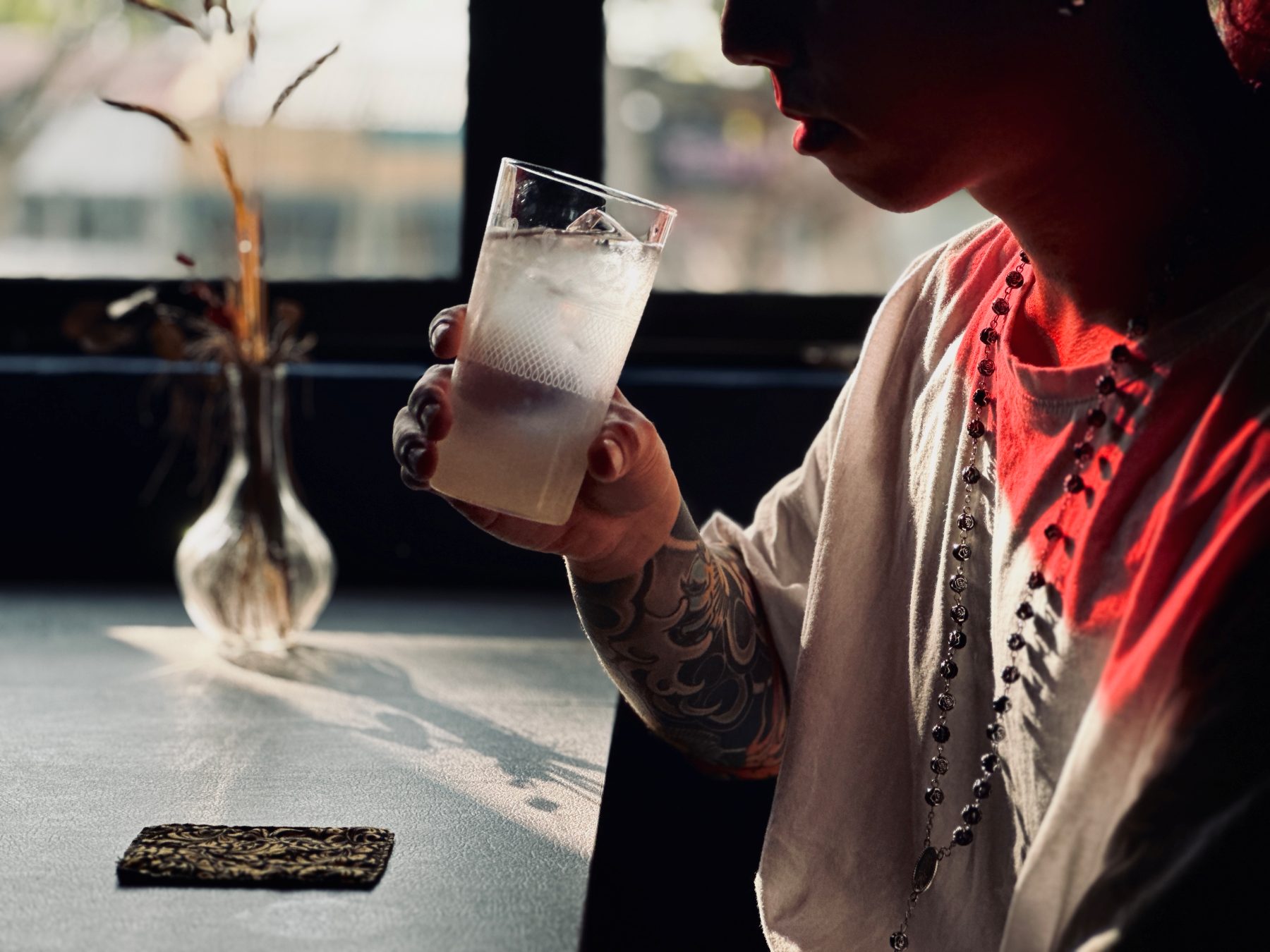 A sunlit highball cocktail held by a person with a sleeve tattoo at Soluble Solids SS2