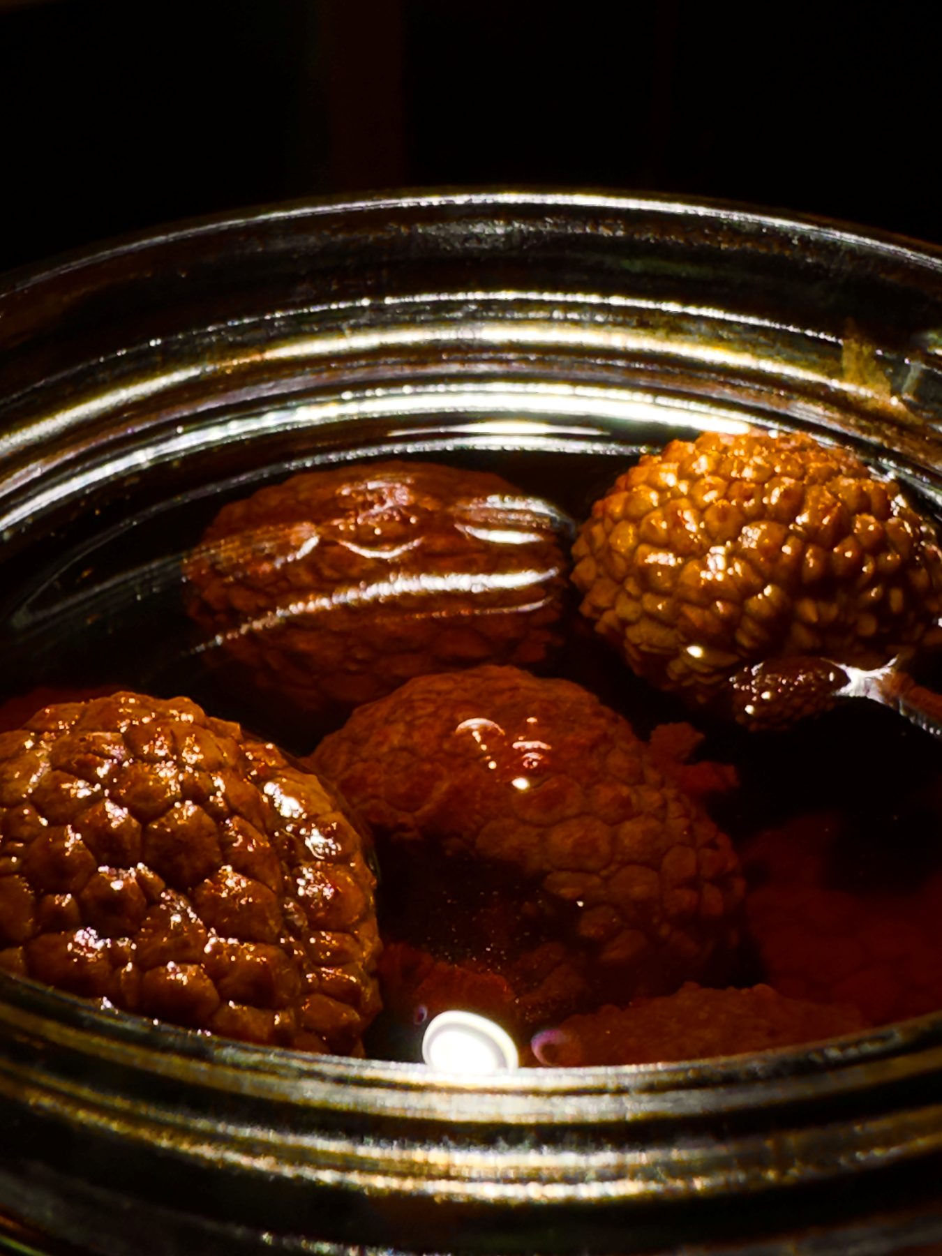 Whole preserved fruit submerged in liquid inside a brass-rimmed container at Soluble Solids
