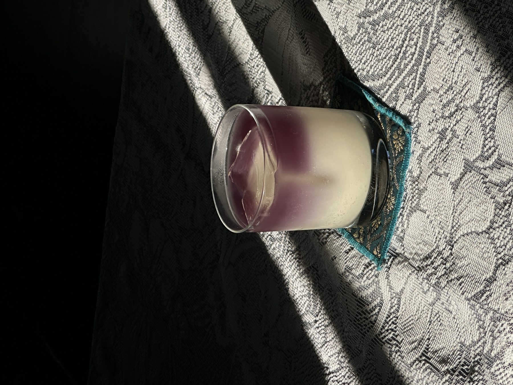 Layered purple-and-white milky cocktail in a rocks glass on patterned lace at Soluble Solids
