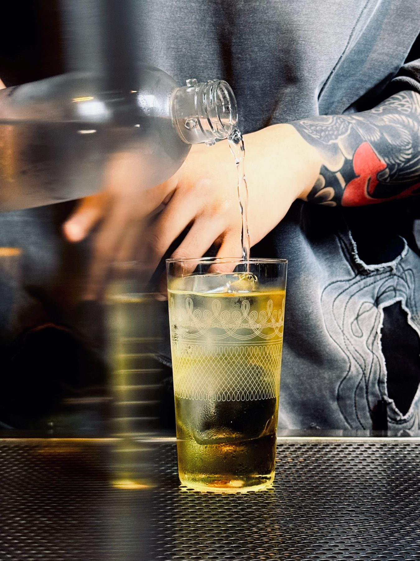 Tattooed bartender pouring a custom cocktail from a large vessel into a vintage etched glass at Soluble Solids SS2