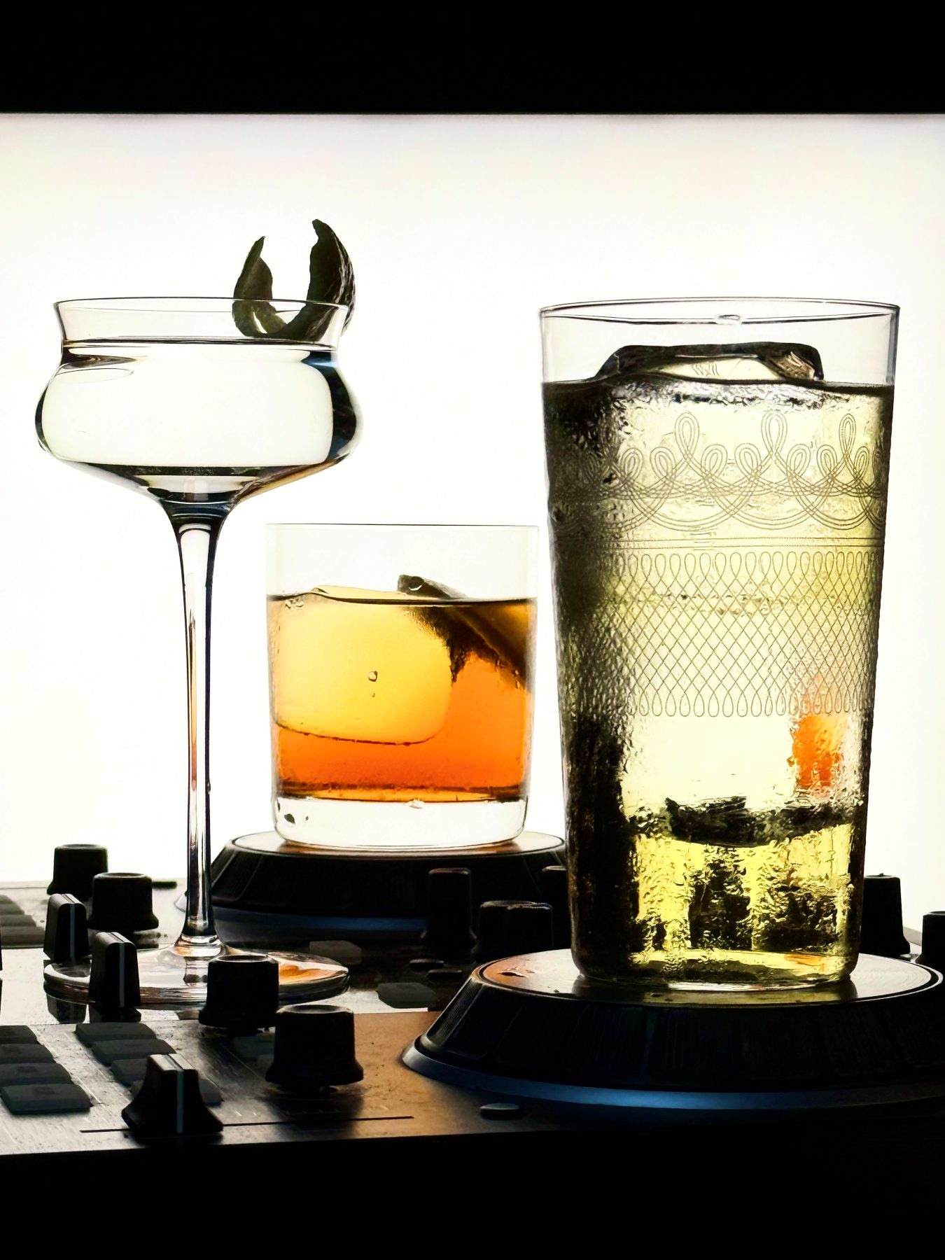 Three custom cocktails - a coupe, a rocks and a highball - lined up on a DJ mixer at Soluble Solids SS2